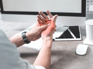 Person seated at desk suffering from thumb and hand pain.