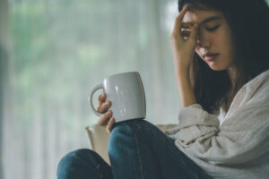 A woman holding a mug and pinching her face in distress.